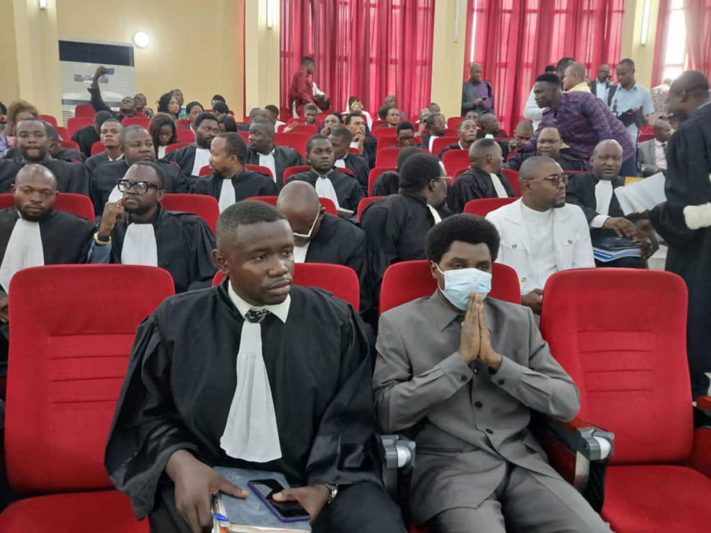 Constant Mutamba (au centre, en costume) entouré de ses avocats lors de l’audience du 23 juillet 2025 devant la Cour de cassation à Kinshasa. Ce jour-là, le tribunal a rejeté les exceptions de procédure soulevées par la défense et a entamé l’examen des faits reprochés au prévenu